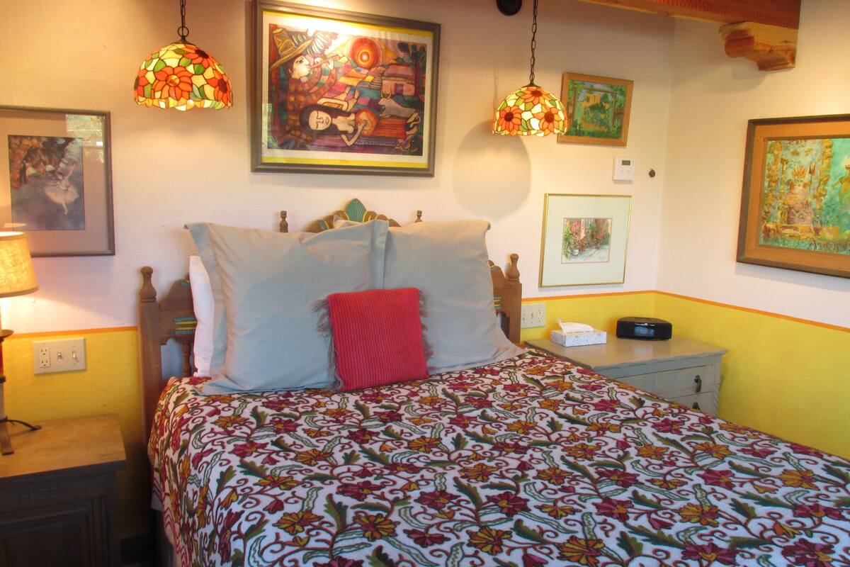 Une chambre à coucher avec un lit, une table de chevet, une lampe et des œuvres d’art murales.