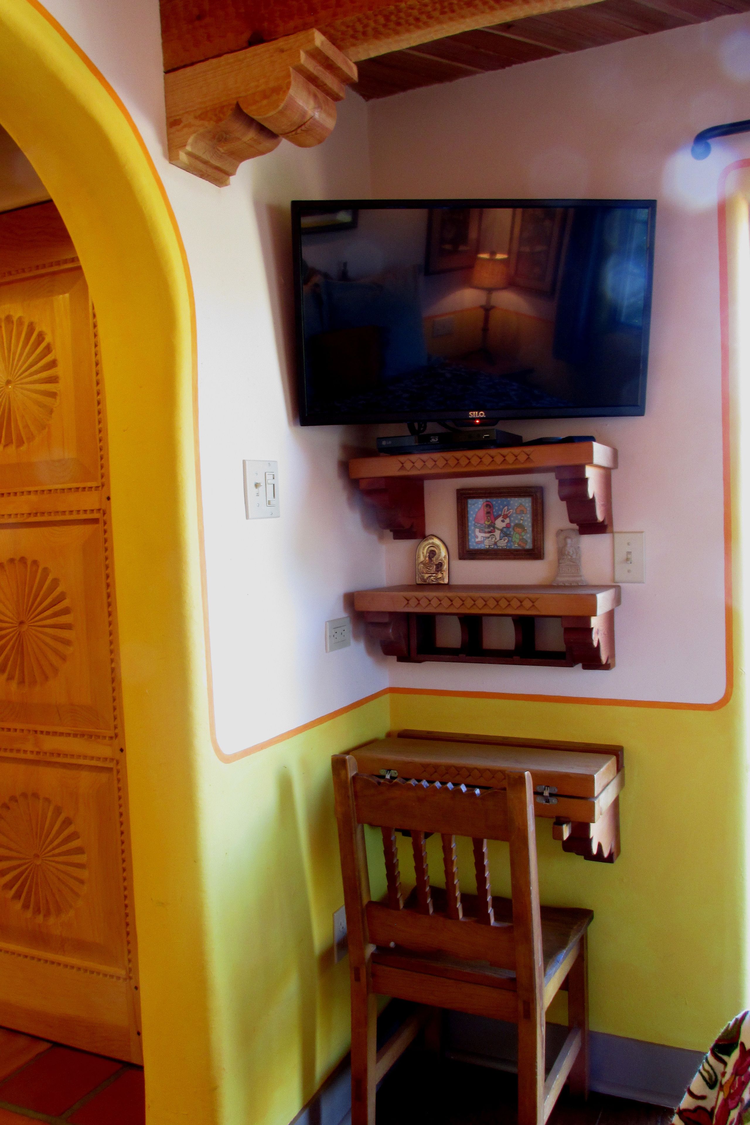 A room with a television mounted on the wall, a wooden chair, and a decorative shelf with a framed picture.