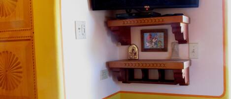 A room with a television mounted on the wall, a wooden chair, and a decorative shelf with a framed picture.