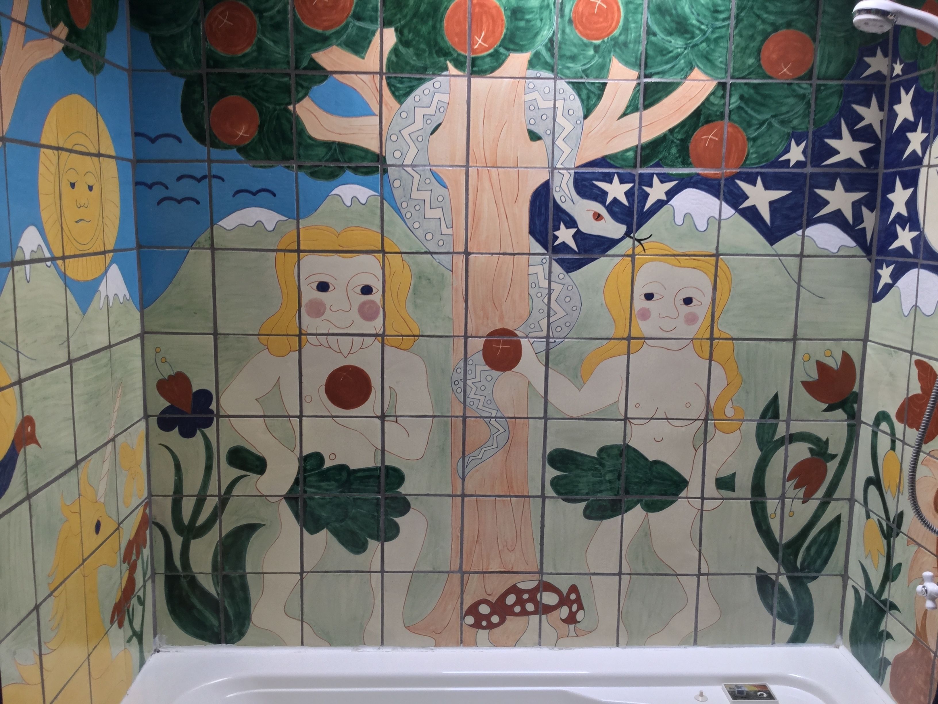 Un mur recouvert de carreaux, orné d’une fresque colorée représentant un arbre, deux personnages et diverses plantes.