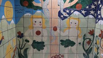 Un mur recouvert de carreaux, orné d’une fresque colorée représentant un arbre, deux personnages et diverses plantes.