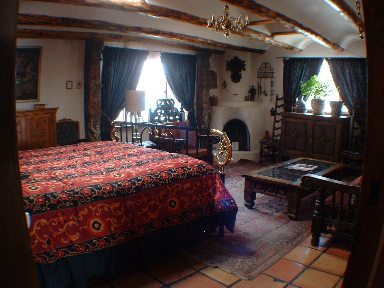A traditional room with a large bed, a fireplace, a dining table, and a chandelier.