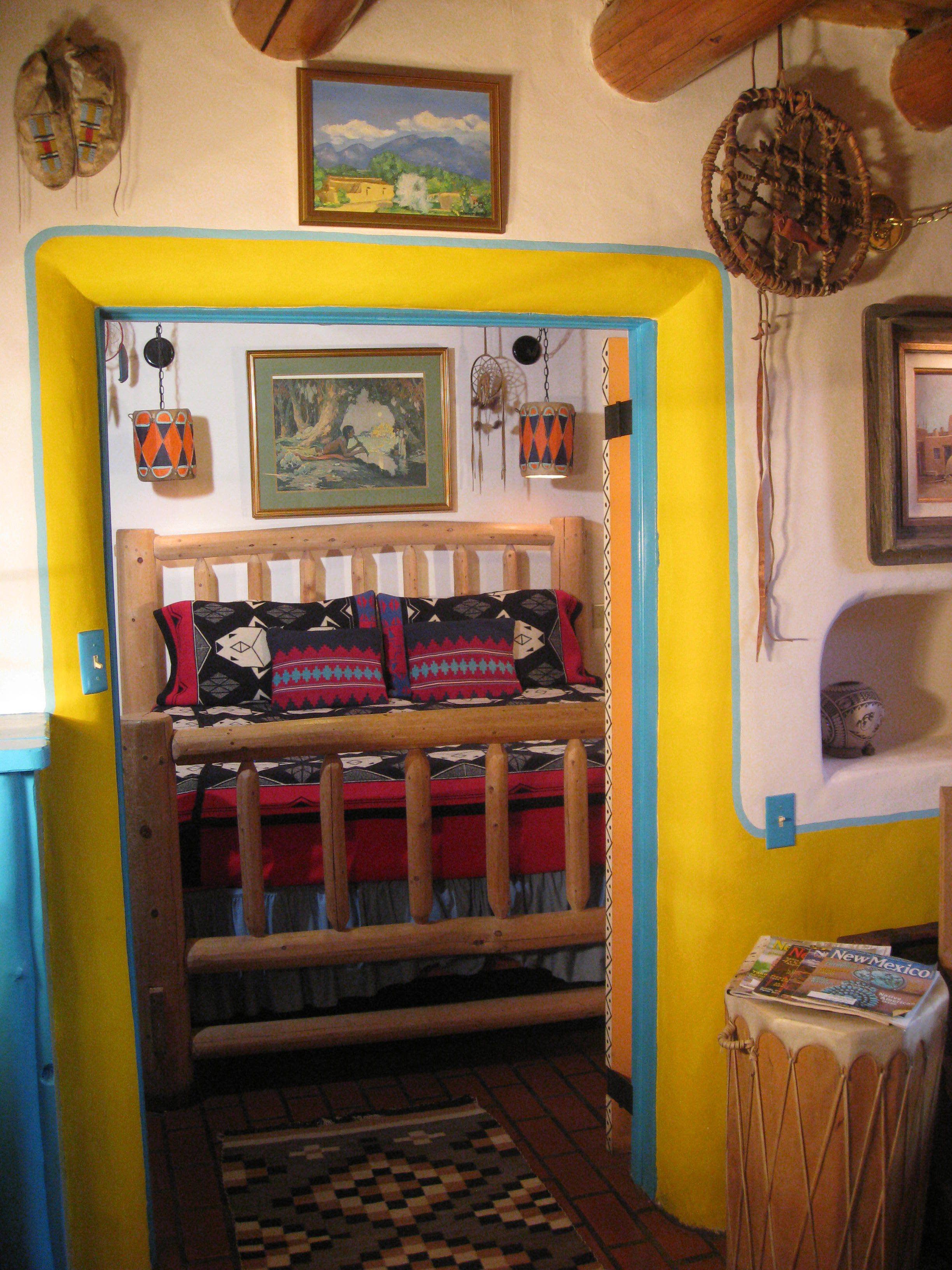 A room with a wooden bed, colorful pillows, a checkered rug, and various wall decorations including paintings and dreamcatchers.