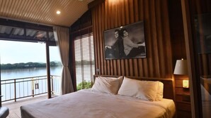Camera da letto con un letto grande, una ventola a soffitto, un comodino, una lampada e vista su un corpo d'acqua tramite ampie finestre.