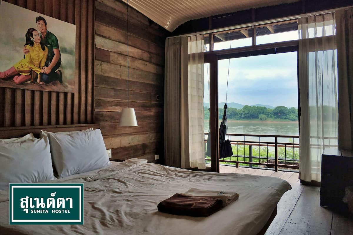 A bedroom with a large bed, a painting on the wall, and a view of a river and greenery.