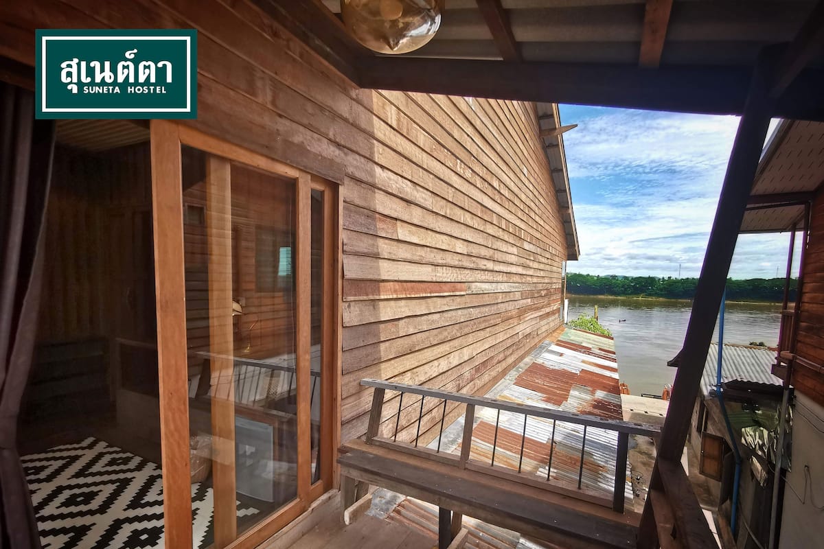 A wooden deck with a glass door leading to a room, a bench, and a view of a river.