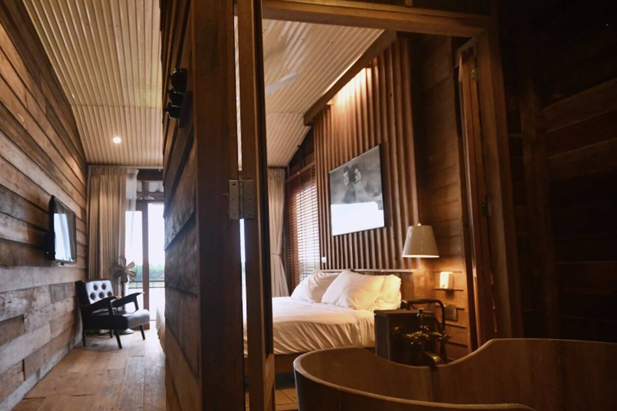 A wooden interior with a bed, a chair, and a bathtub.