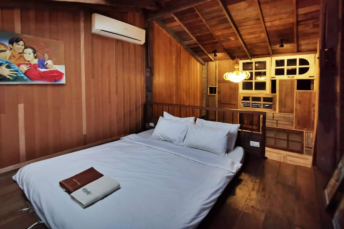 A wooden room with a bed, an air conditioning unit, and a painting on the wall.