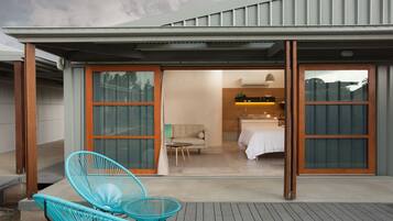 Una casa moderna con un porche cubierto, dos sillas turquesas, y una habitación visible a través de las puertas correderas.
