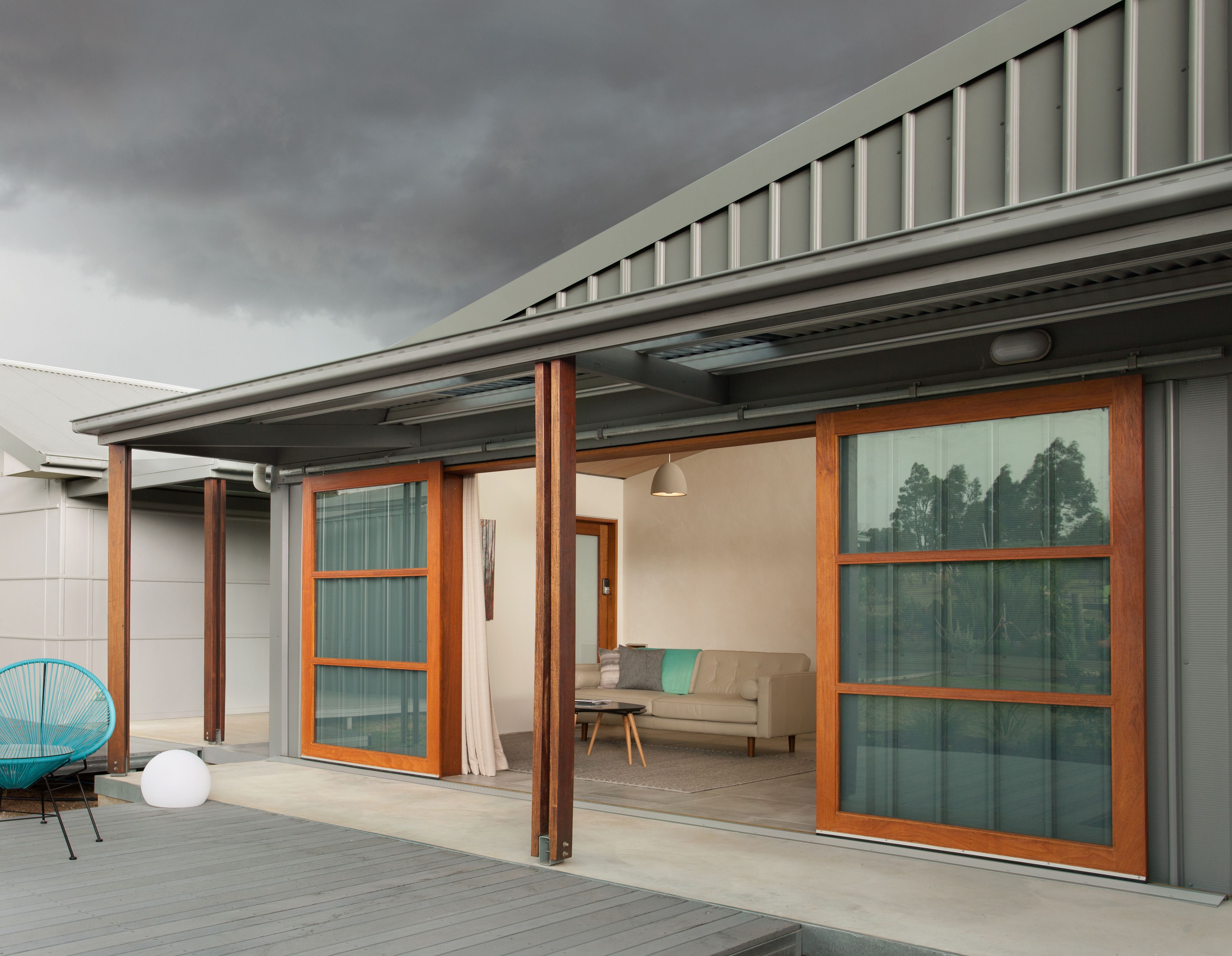 Ein modernes Haus mit großen Schiebeglastüren, einer Holterrasse und einem gemütlichen Innenraum mit Sofa und Tisch.