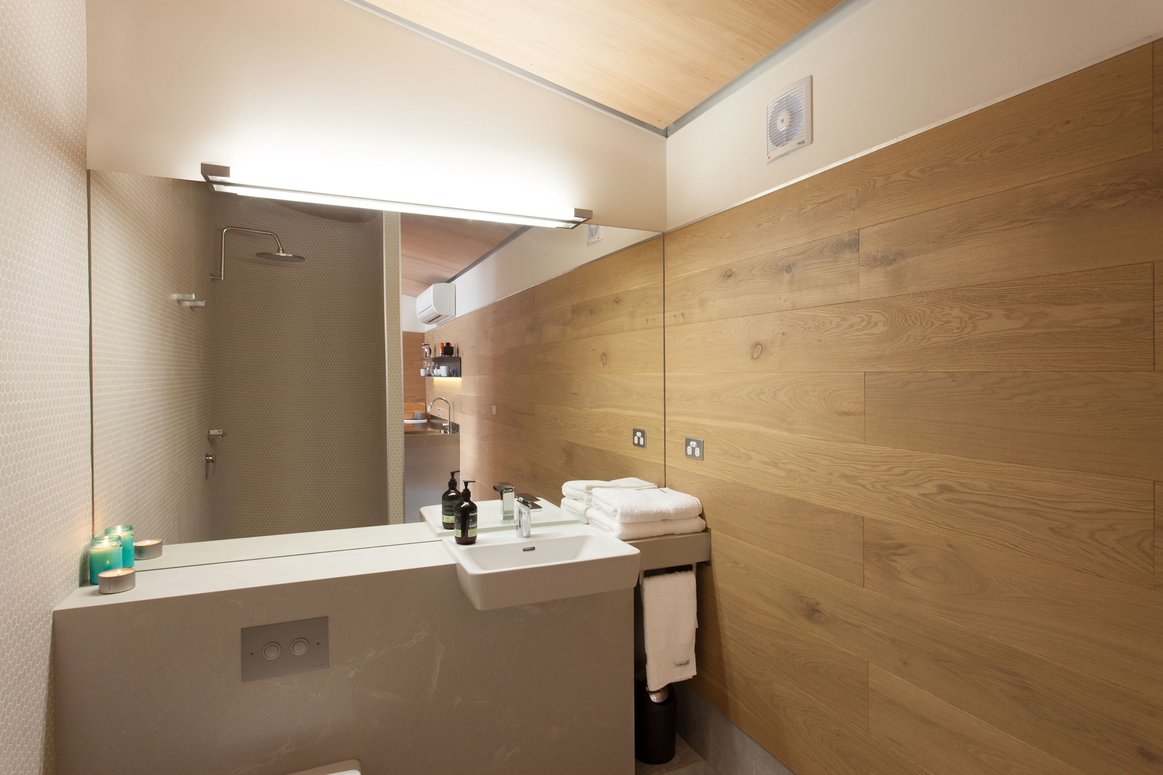 Un baño moderno con pared de madera, un espejo grande, un lavamanos con artículos de tocador y una ducha.