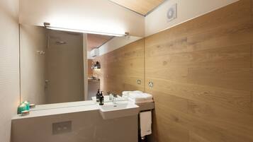 Un baño moderno con pared de madera, un espejo grande, un lavamanos con artículos de tocador y una ducha.