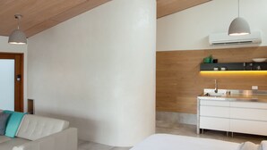 Ein modernes Schlafzimmer mit Deckenventilator, einem weißen Bett, einer Couch und einer Küchenzeile mit Spüle und Arbeitsplatte.