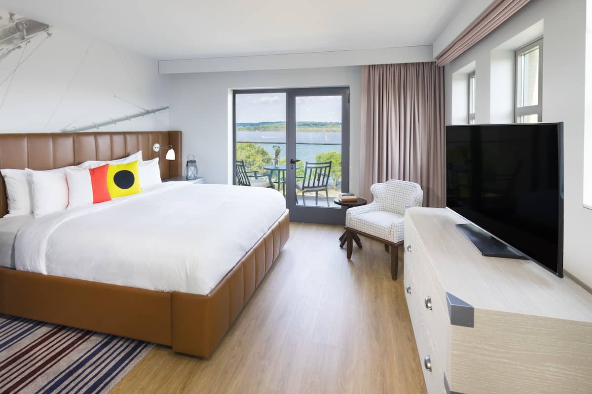 Ett hotellrum med en stor säng, en tv, en balkong med utsikt över vattnet och en stol.