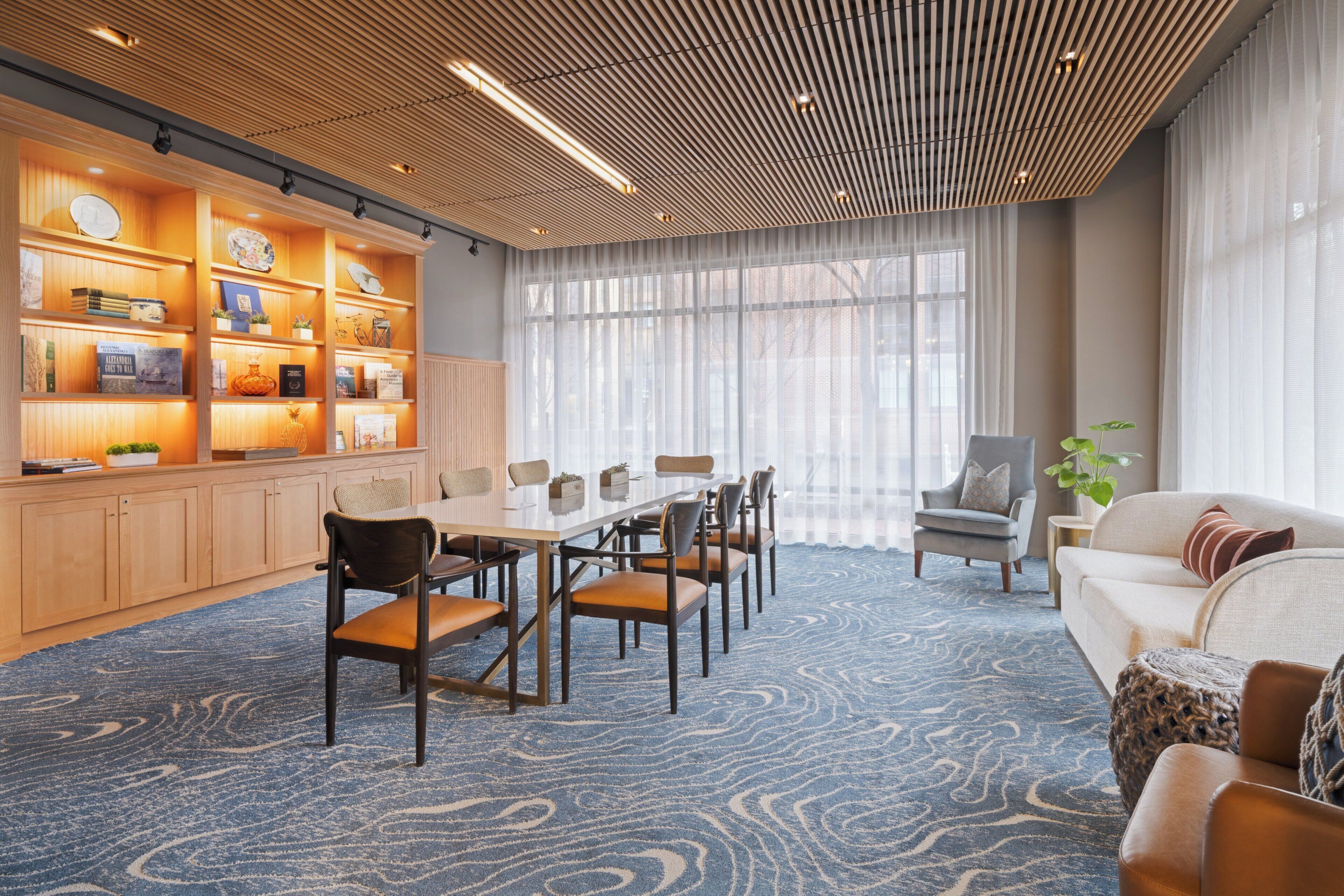 A modern hotel room with a dining area, a sofa, and a bookshelf.