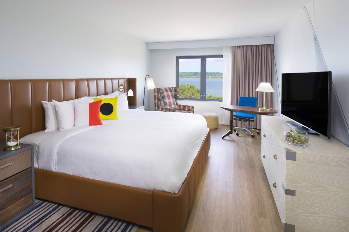Ett hotellrum med en stor säng, ett skrivbord, en tv och utsikt över omgivningarna.
