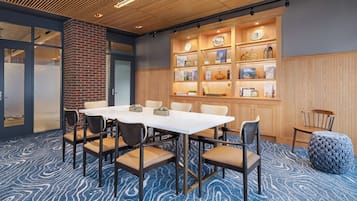 A conference room with a white table, six chairs, a brick wall, and a wooden panel wall with shelves.