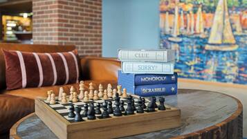 A chessboard on a round wooden table with a stack of board games and a painting in the background.