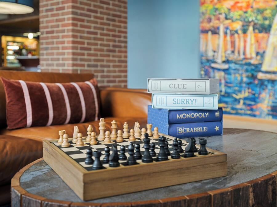 A chessboard on a round wooden table with a stack of board games and a painting in the background.