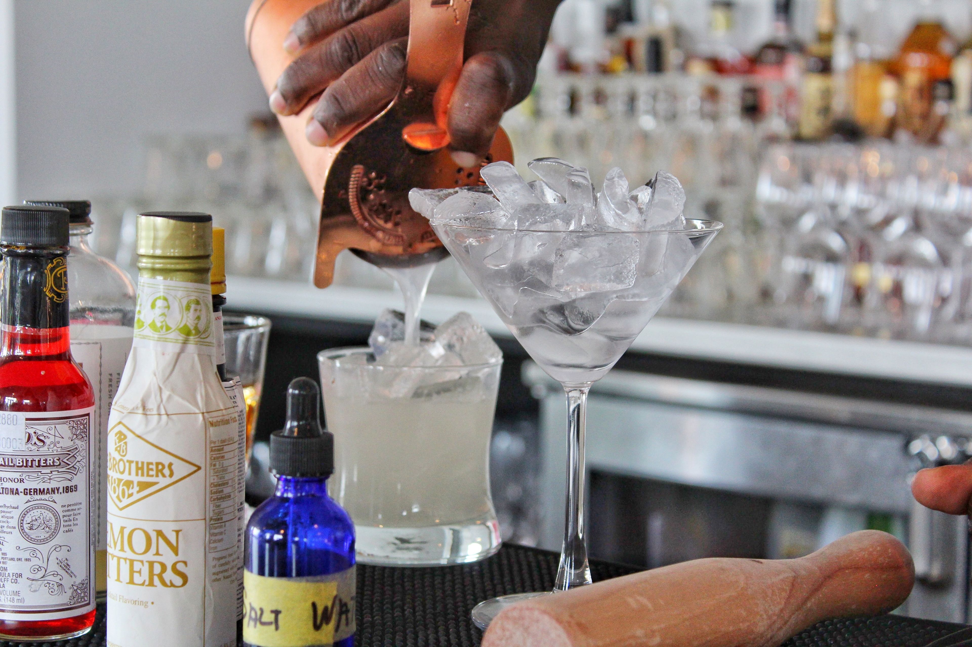 A bartender pouring a drink into a martini glass filled with ice.