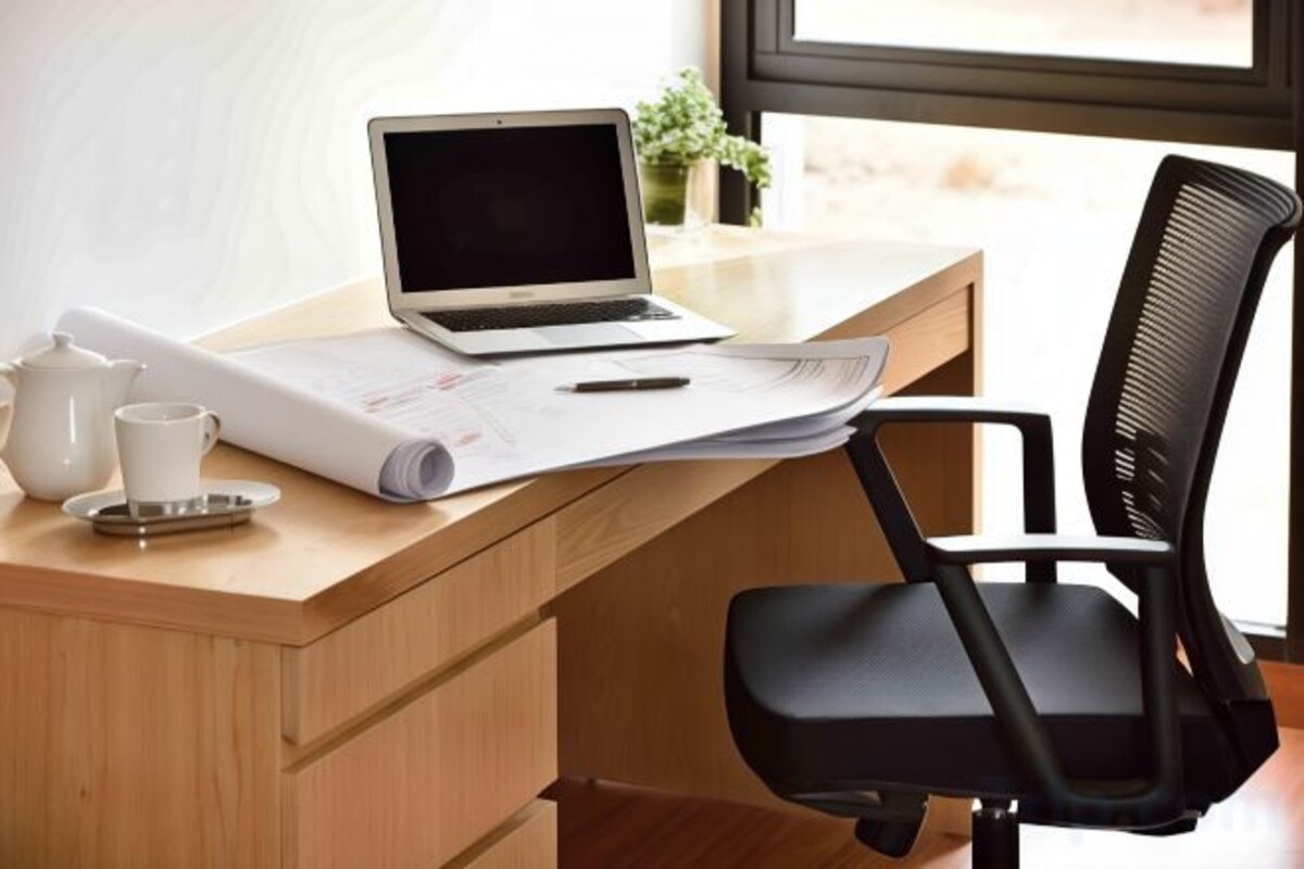 A wooden desk with a laptop, papers, a pen, and a teapot.