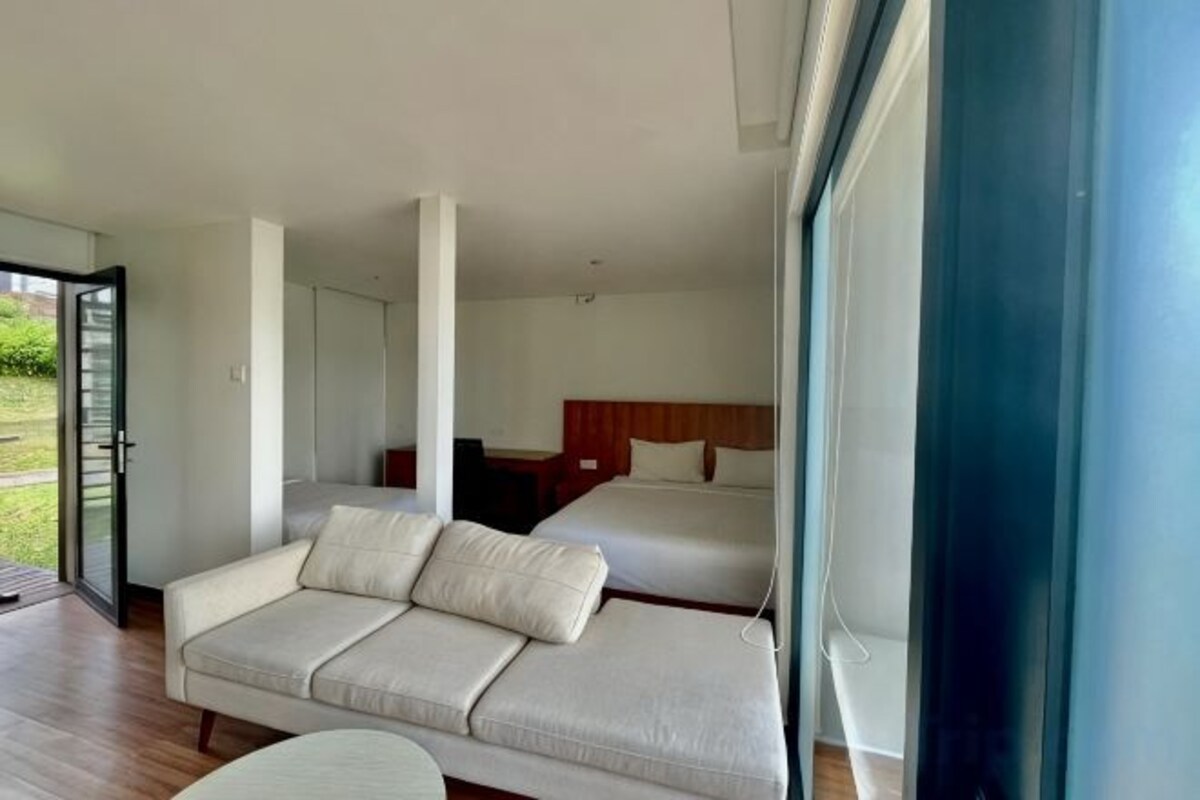 A modern bedroom with a sofa bed, a separate bed, and a large window.