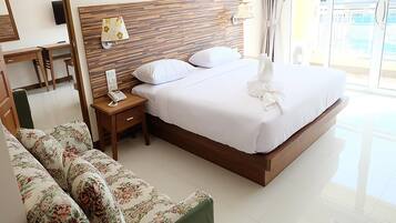 A hotel room with a wooden headboard, a bed with white linens, a floral sofa, a bedside table with a lamp, and a view of the outdoors.