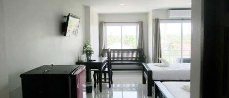 A hotel room with a bed, a desk, a chair, a small refrigerator, and a window with curtains.