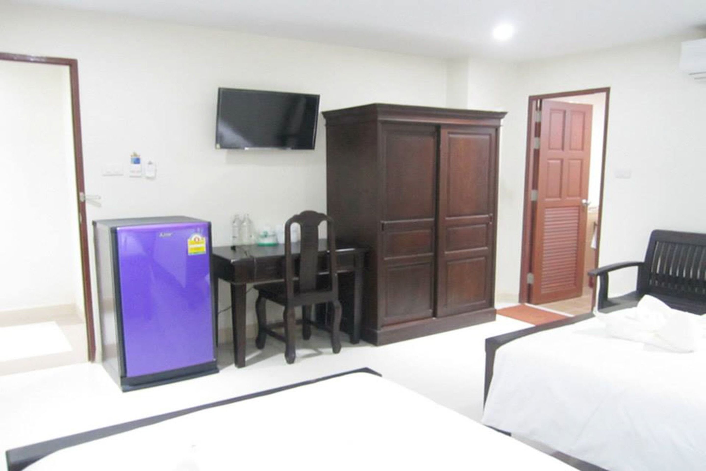 A hotel room with a bed, a desk with a chair, a wardrobe, a television, and a refrigerator.