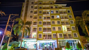 Een meerlaags hotel met balkons, een goed verlichte ingang en palmbomen op de voorgrond.