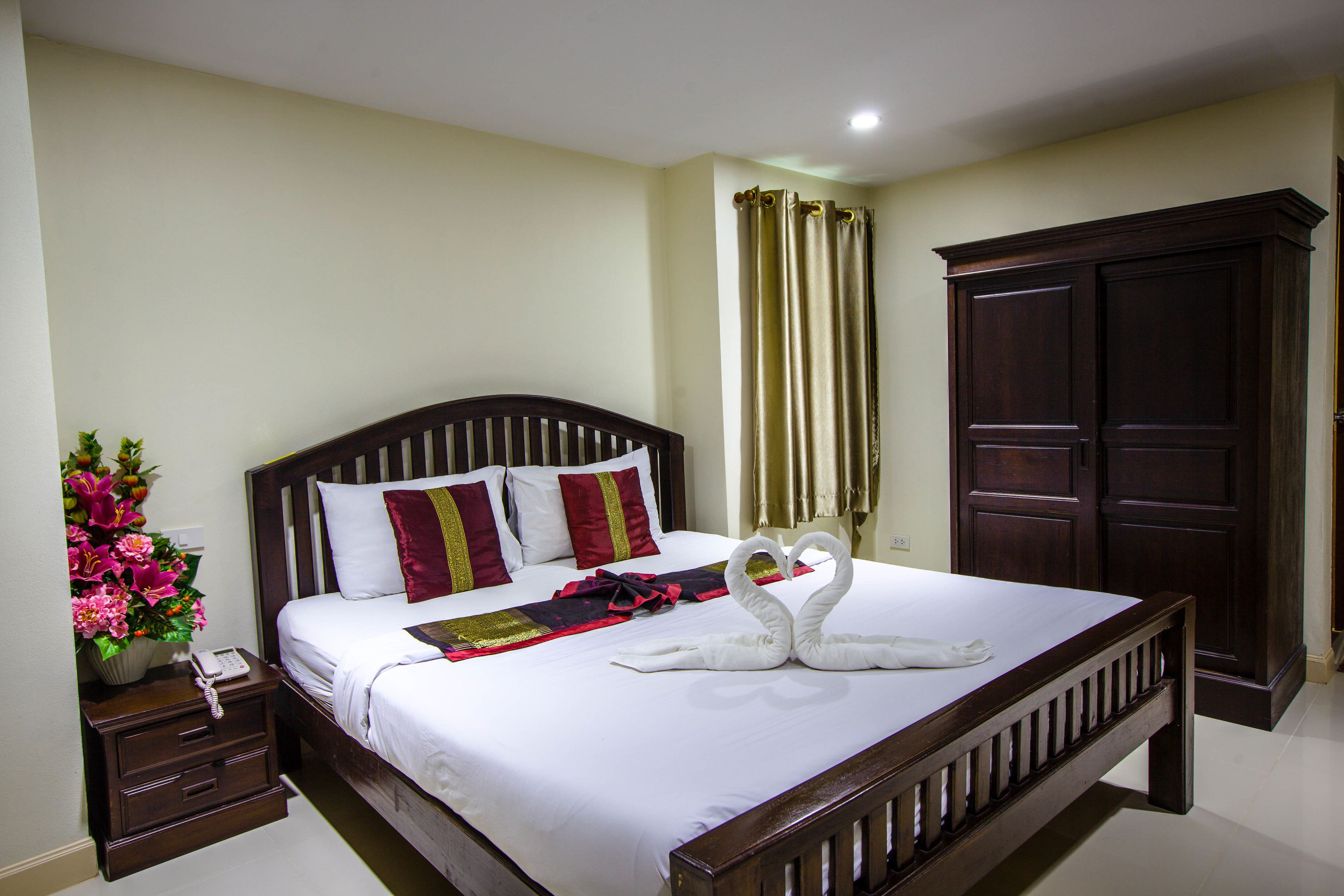 A neatly made bed with a decorative swan towel arrangement, a bedside telephone, and a floral vase on a nightstand.