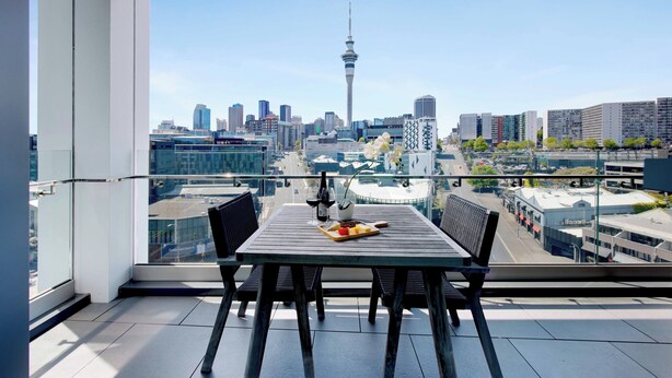A balcony with a table set for two, overlooking a cityscape with a prominent tower.