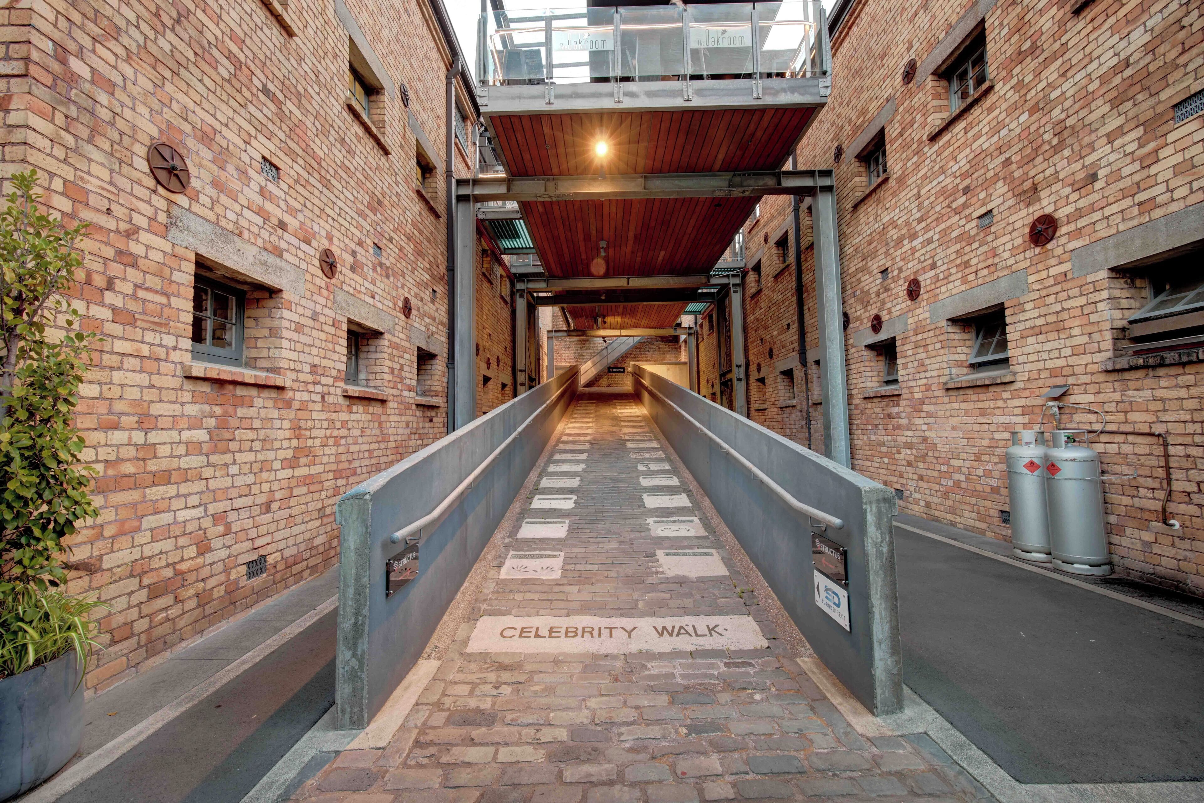 A brick-walled alleyway with a wooden ceiling and a metal walkway labeled "CELEBRITY WALK."