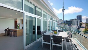 A modern hotel room with a balcony, large windows, and a view of a city skyline including a tower.