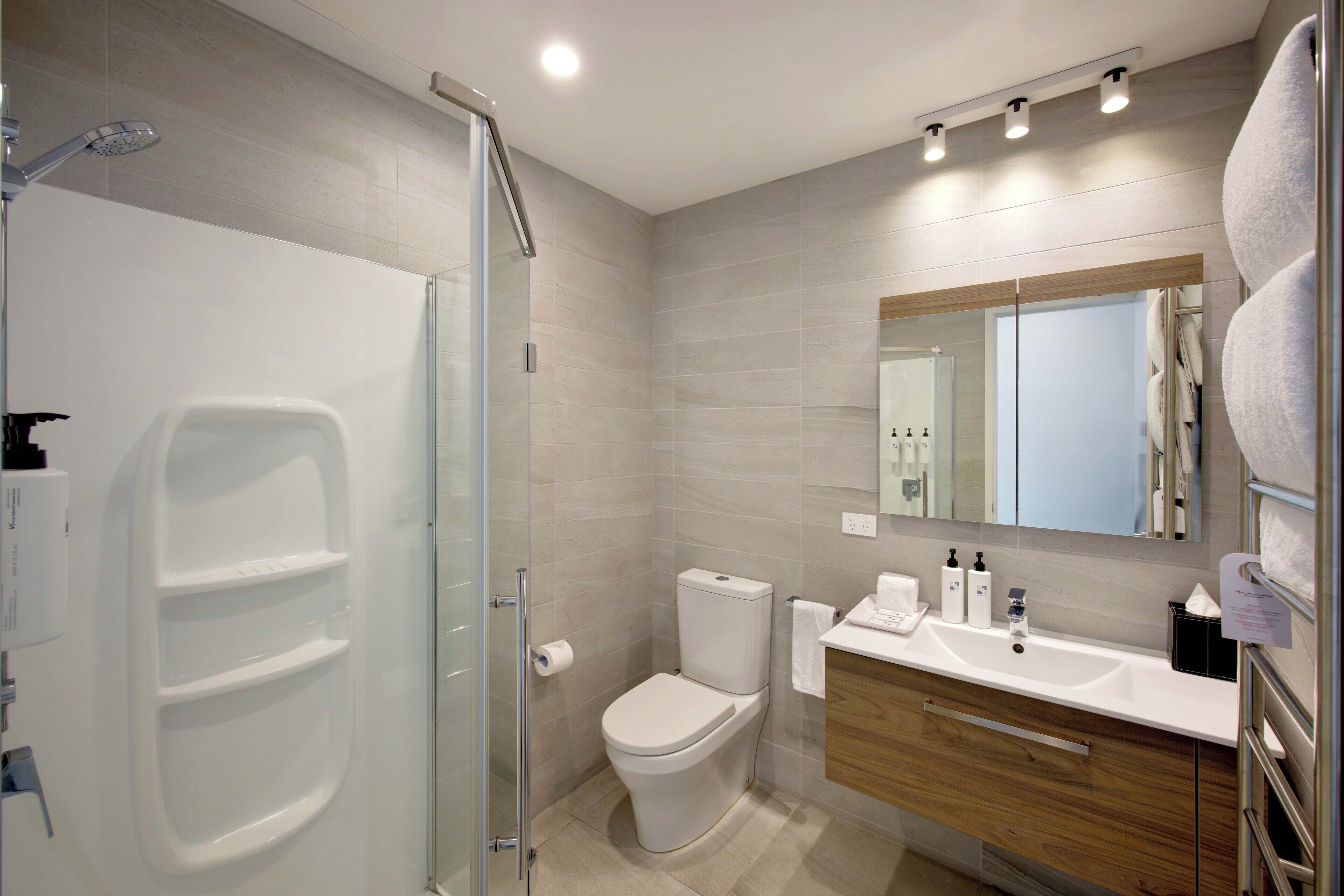 Une salle de bain moderne avec une douche à parois de verre, des toilettes, un lavabo avec des articles de toilette et un miroir.