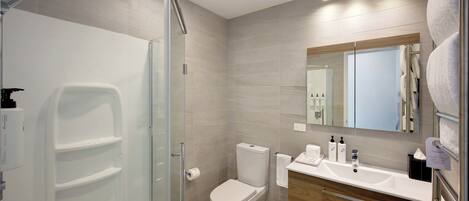 Une salle de bain moderne avec une douche à parois de verre, des toilettes, un lavabo avec des articles de toilette et un miroir.