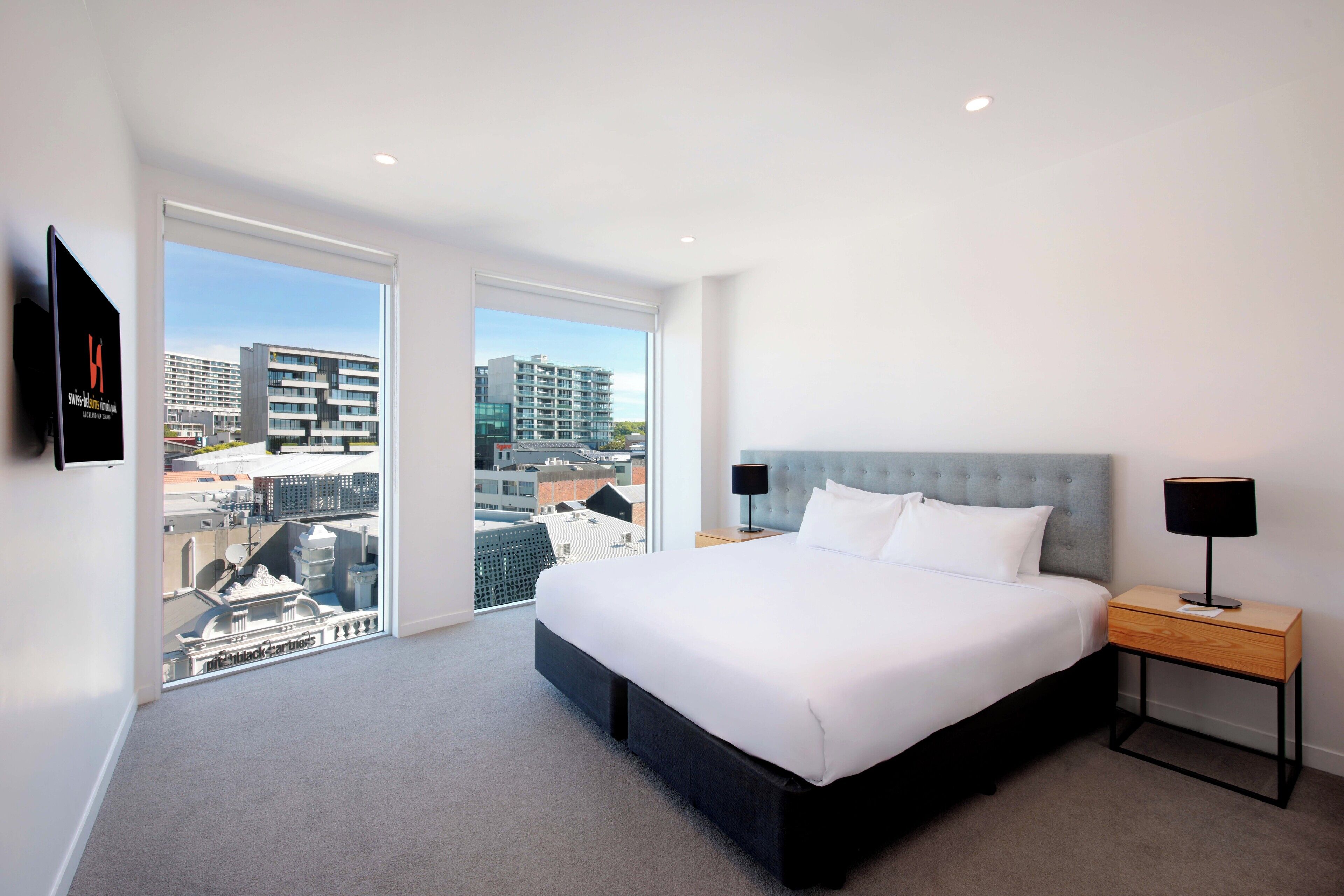 A modern hotel room with a large bed, a TV mounted on the wall, and a balcony with a city view.