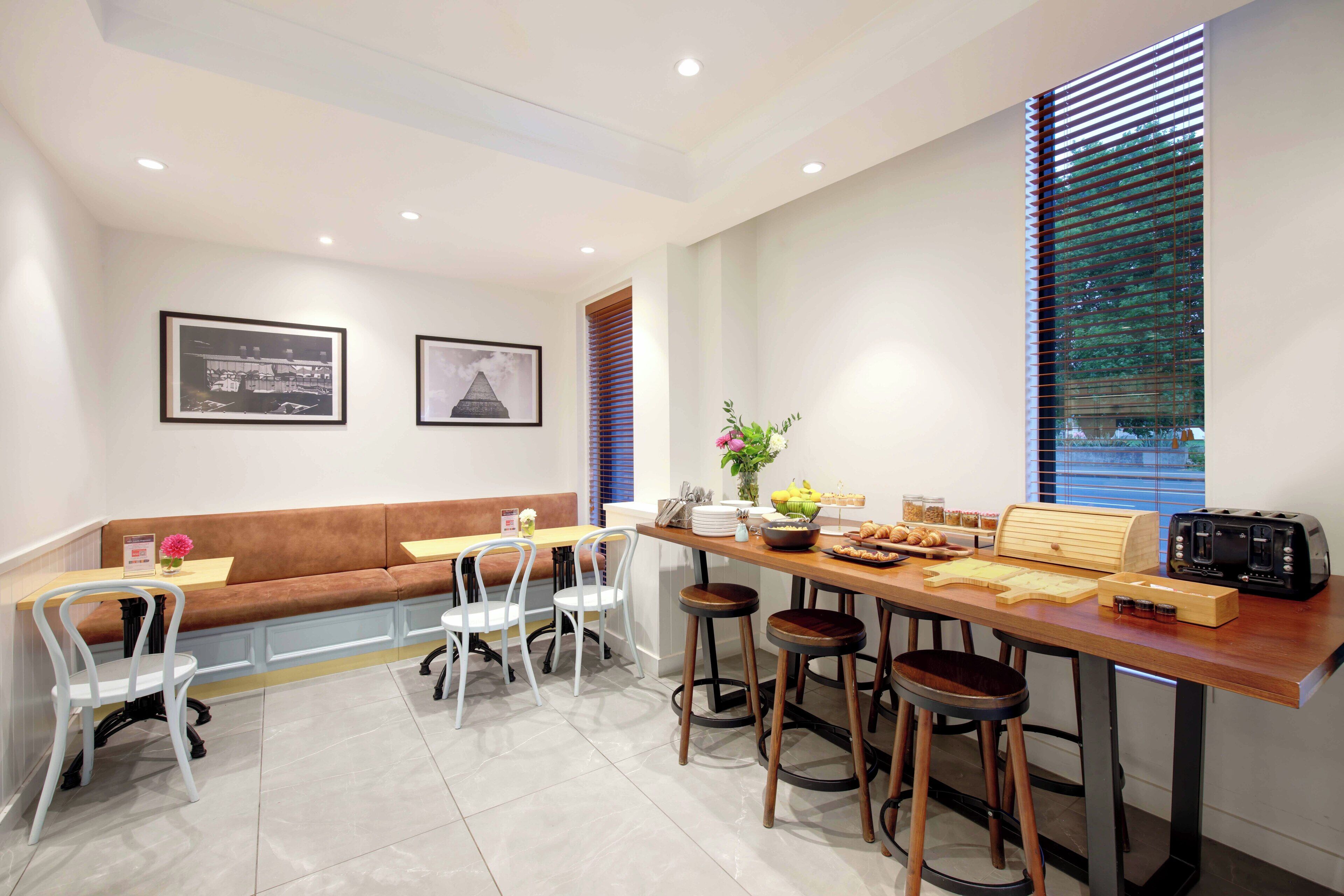 A modern dining area with a wooden table, bar stools, a bench, and framed pictures on the wall.