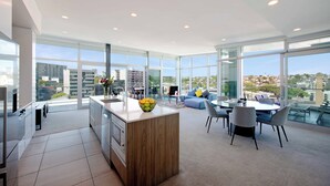 A modern apartment with a kitchen, dining area, and living room with large windows offering city views.