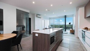 A modern kitchen with a central island, a dining area with a round table, and a large window offering a view of the outdoors.