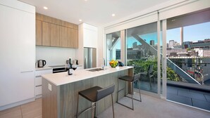 A modern kitchen with a large island, bar stools, and a city view through large windows.