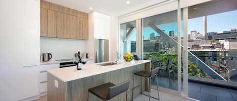 A modern kitchen with a large island, bar stools, and a city view through large windows.