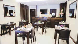 A hotel dining area with multiple tables and chairs, a reception desk, and a large mirror on the wall. - Winzelle Suites (Zamboanga)