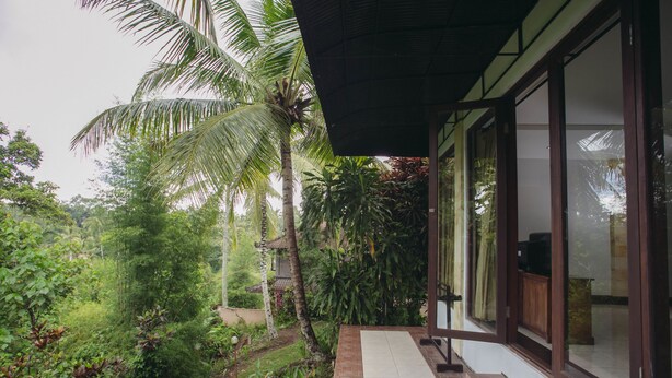 A covered outdoor area with a brick pathway, surrounded by lush greenery and a palm tree. - Bucu Beji Ubud (Ubud)