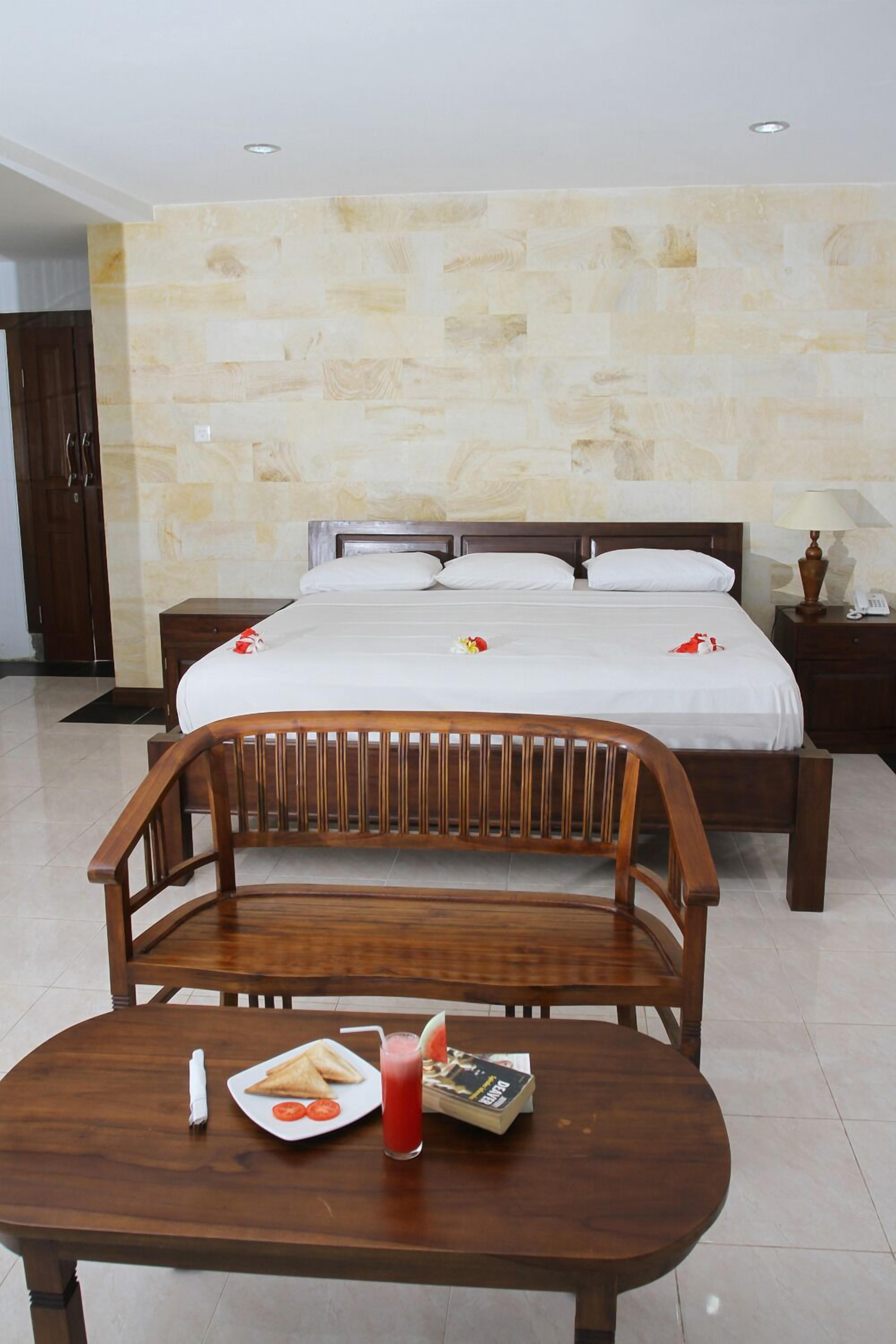 A hotel room with a bed, a wooden bench, a table with breakfast, and a stone wall.