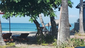 Un área de descanso frente a la playa con sillones y una estructura de techo de paja.