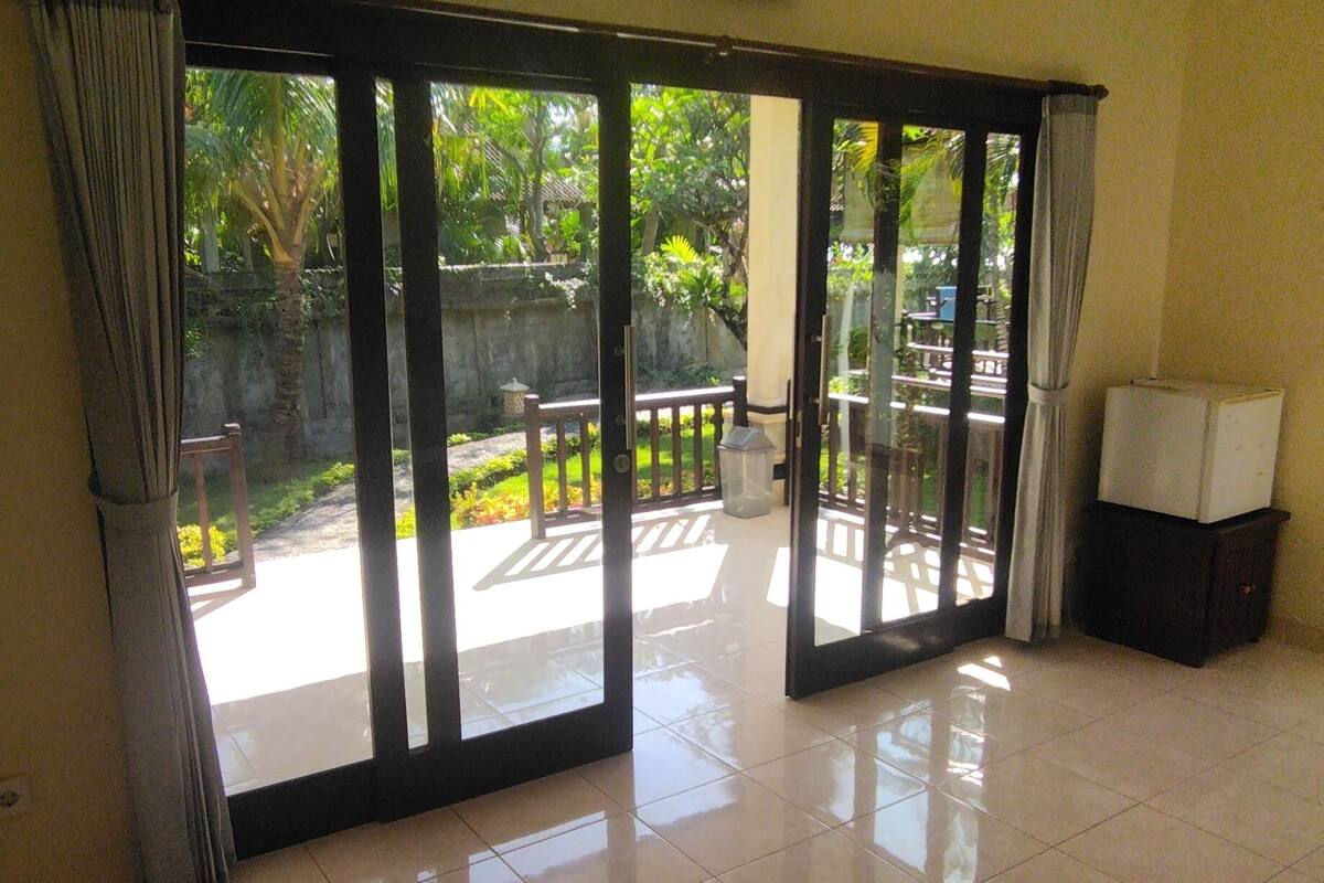 A spacious room with a large sliding glass door leading to an outdoor area with a bench and greenery.