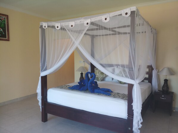 A bed with a canopy, a nightstand with a lamp, and a wall with a painting.