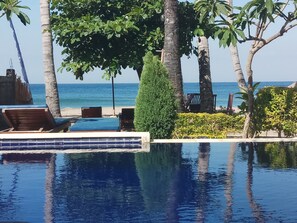 A pool area with lounge chairs, a small pool, and a view of the sea.