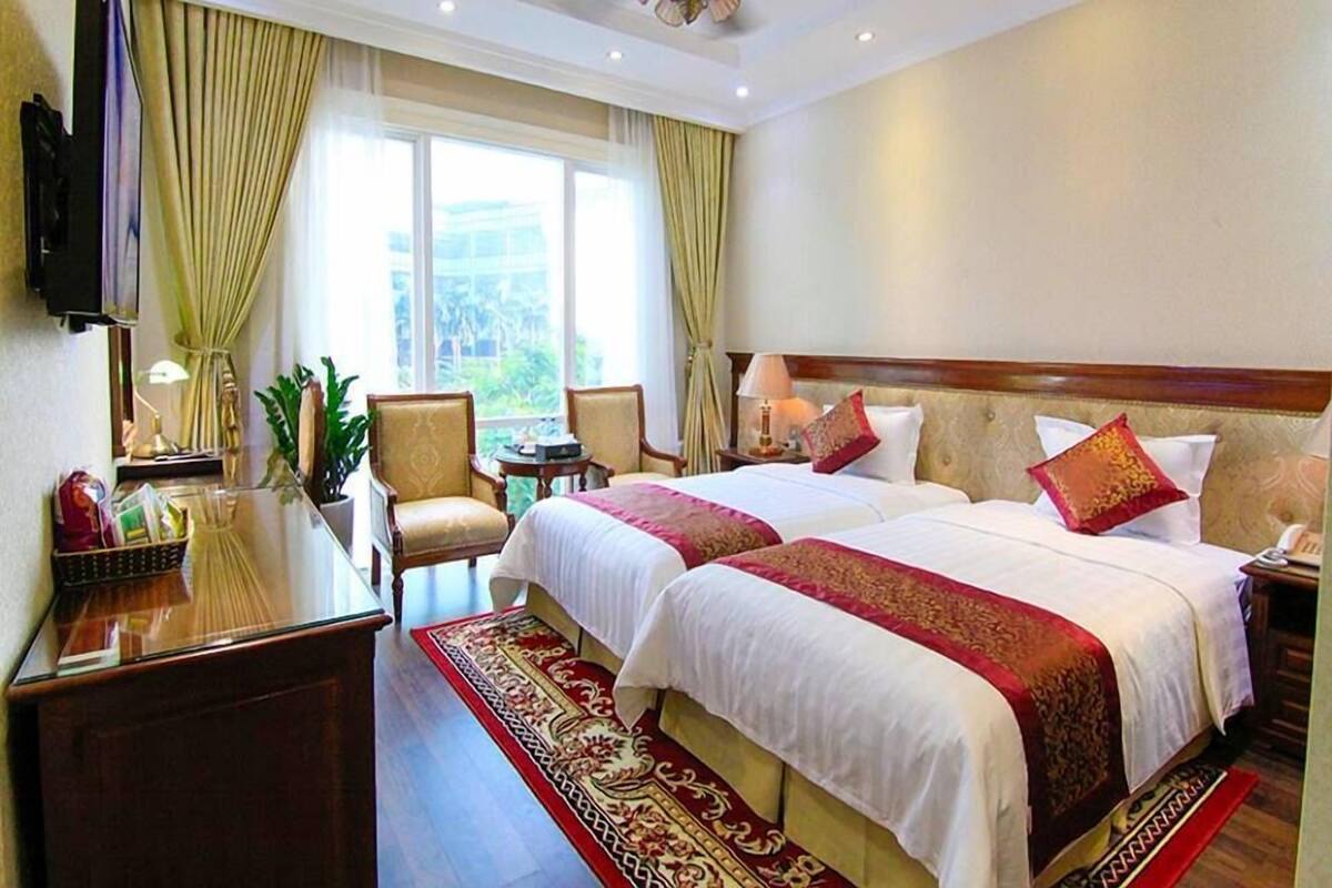 Habitación de hotel con dos camas, un escritorio, un televisor y un ventanal con cortinas.